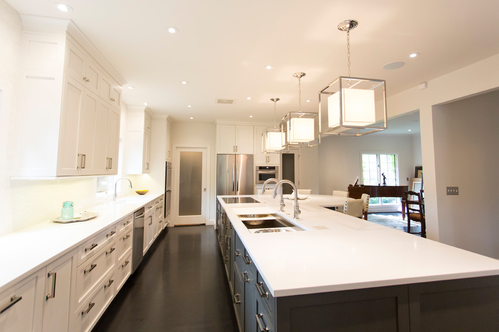 Example of a large transitional l-shaped dark wood floor and brown floor kitchen design with an undermount sink, shaker cabinets, white cabinets, quartz countertops, white backsplash, stainless steel appliances, an island and white countertops