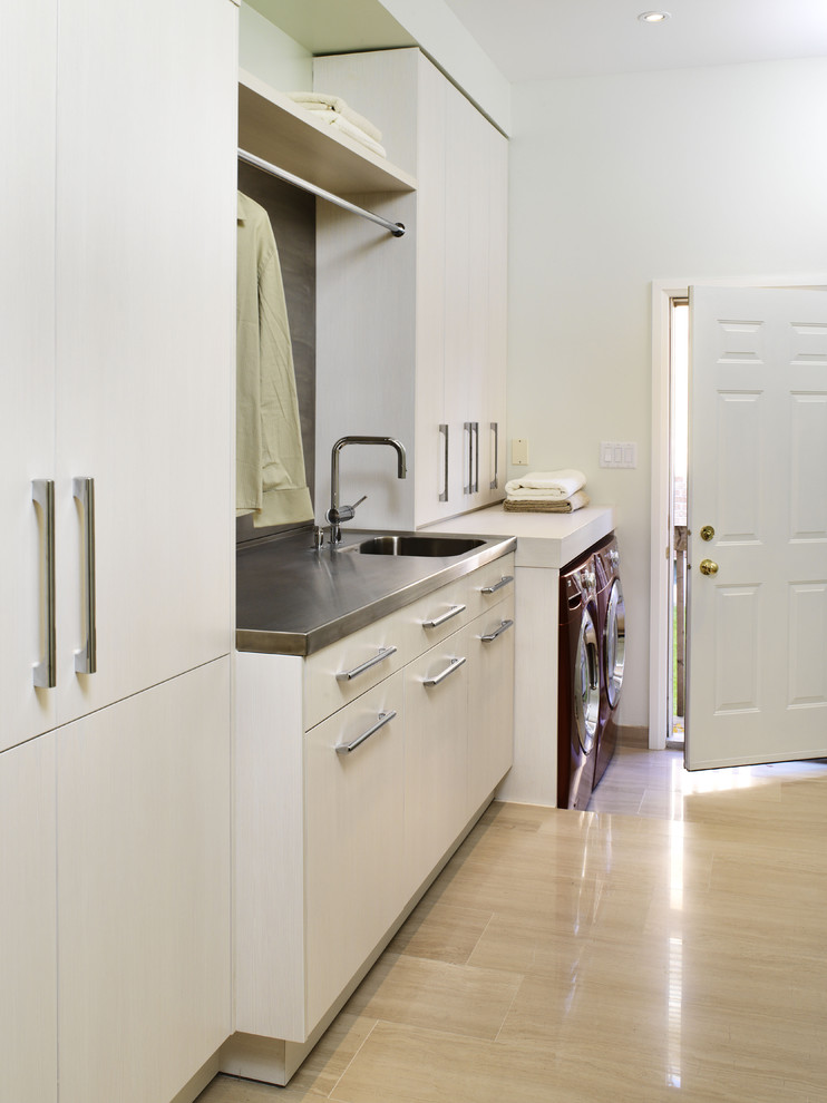 Contemporary laundry room in Toronto with stainless steel benchtops, limestone floors, a side-by-side washer and dryer, beige floor, white cabinets, an integrated sink and white walls.