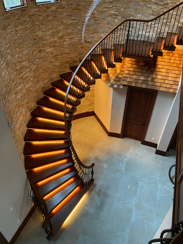 На фото: изогнутая лестница в классическом стиле с деревянными ступенями, деревянными перилами и кирпичными стенами без подступенок