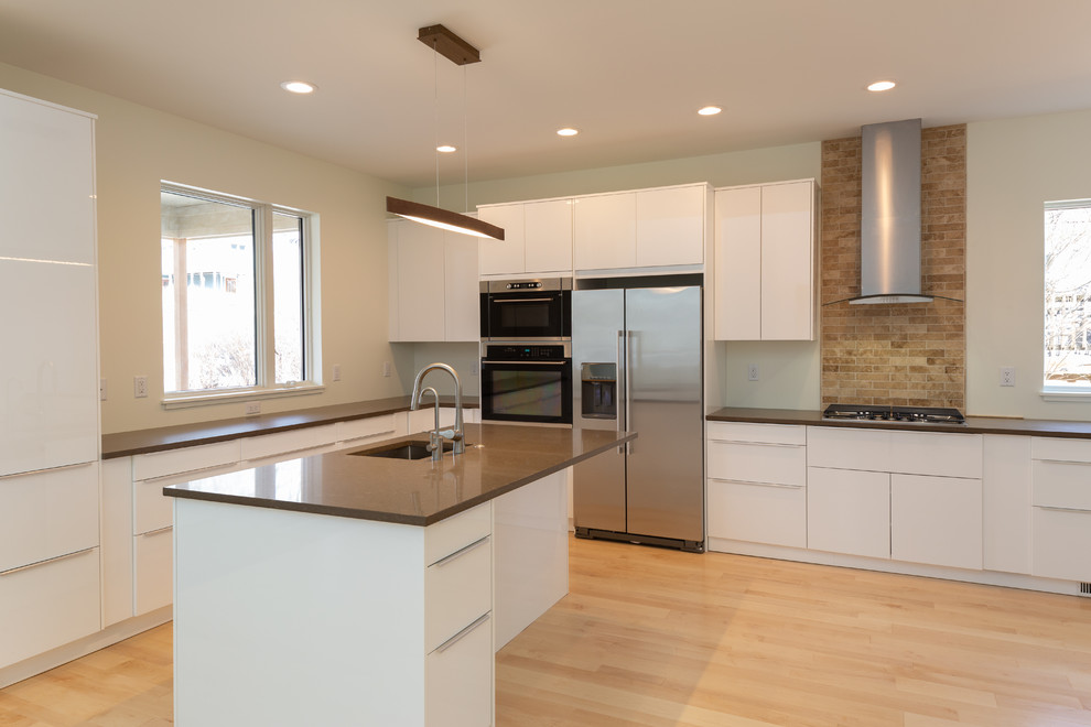 Inspiration for a mid-sized modern l-shaped eat-in kitchen in Detroit with an undermount sink, flat-panel cabinets, white cabinets, quartz benchtops, stainless steel appliances, light hardwood floors, with island, white benchtop, beige splashback, porcelain splashback and brown floor.