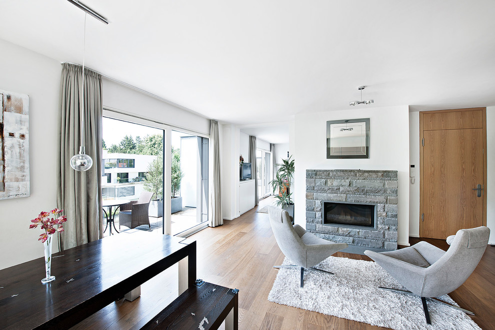 This is an example of a small contemporary open concept living room in Munich with white walls, medium hardwood floors, a two-sided fireplace and a stone fireplace surround.