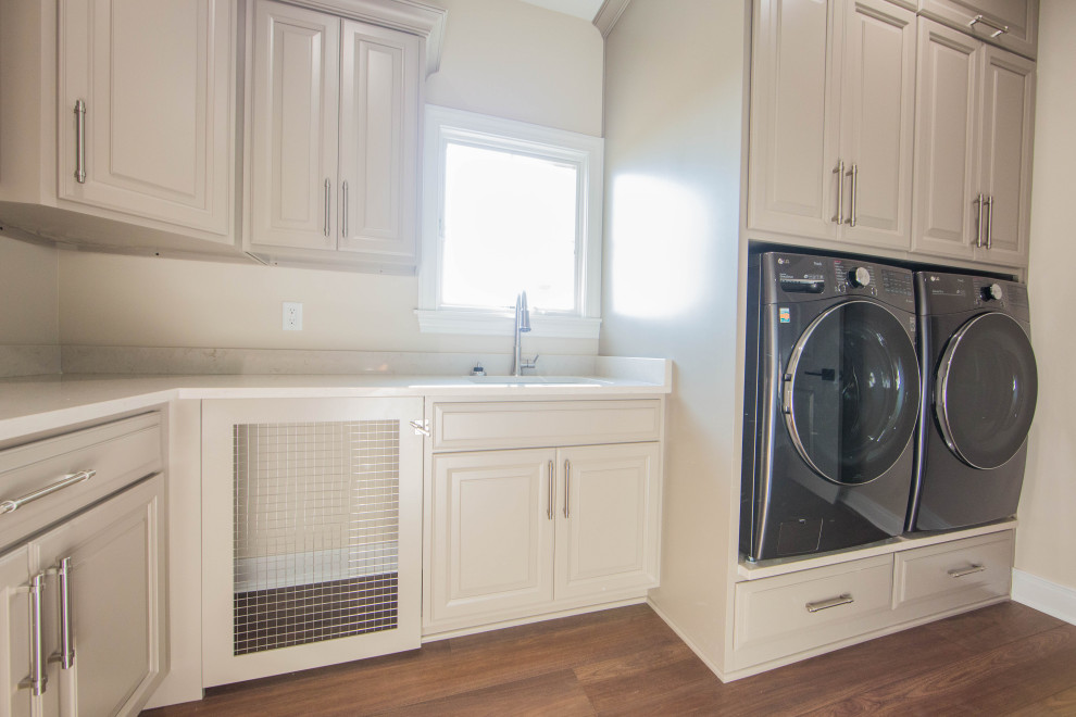This is an example of a large contemporary l-shaped dedicated laundry room in Indianapolis with an undermount sink, raised-panel cabinets, grey cabinets, granite benchtops, beige walls, medium hardwood floors, an integrated washer and dryer, brown floor and multi-coloured benchtop.
