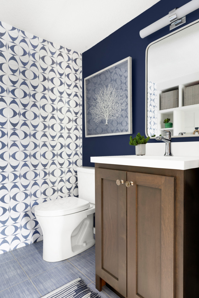 Photo of a small beach style cloakroom in Minneapolis with shaker cabinets, medium wood cabinets, a two-piece toilet, blue tiles, ceramic tiles, blue walls, porcelain flooring, an integrated sink, solid surface worktops, blue floors, white worktops and a freestanding vanity unit.