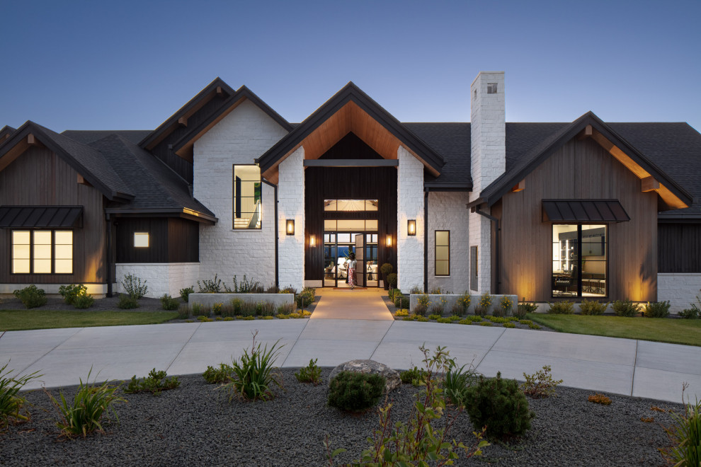 Award-Winning Luxury Custom Home | Modern + Traditional Interior Design | Lone T - The front entry of this luxury custom home is striking, with traditional roofline and modern materials on the facade. White stone, light wood paneling, black steel awnings, and a grand steel and wood door framed in windows.