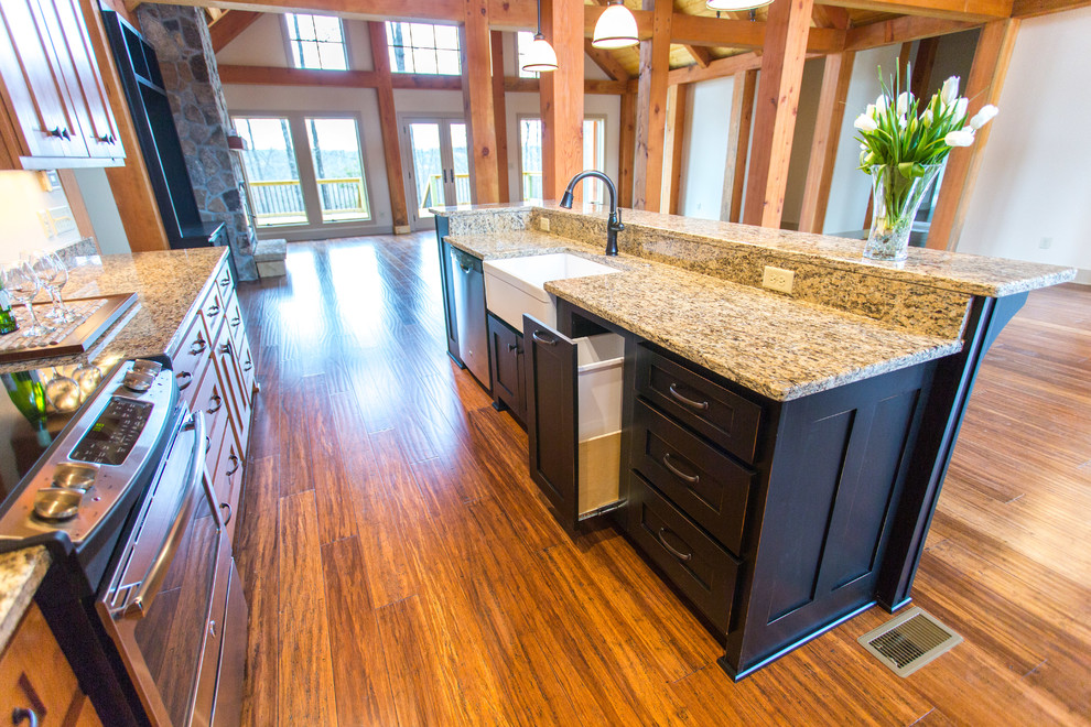 Open concept kitchen - large rustic l-shaped medium tone wood floor open concept kitchen idea with a farmhouse sink, shaker cabinets, medium tone wood cabinets, granite countertops, stainless steel appliances and an island