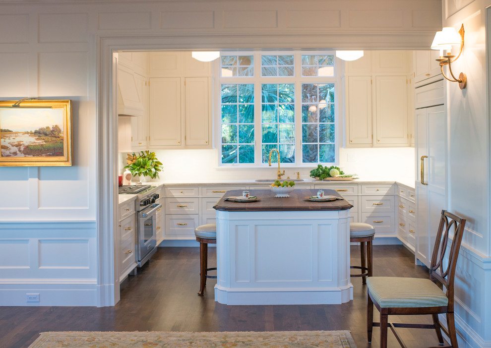 Mid-sized traditional u-shaped open plan kitchen in Charleston with an undermount sink, recessed-panel cabinets, white cabinets, granite benchtops, white splashback, terra-cotta splashback, stainless steel appliances, medium hardwood floors, with island, brown floor and white benchtop.