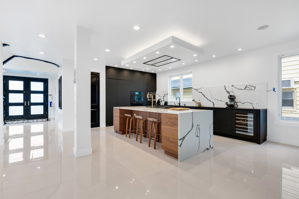 This is an example of an expansive contemporary single-wall eat-in kitchen in New York with a double-bowl sink, flat-panel cabinets, black cabinets, marble benchtops, white splashback, stone slab splashback, coloured appliances, marble floors, with island, white floor and black benchtop.