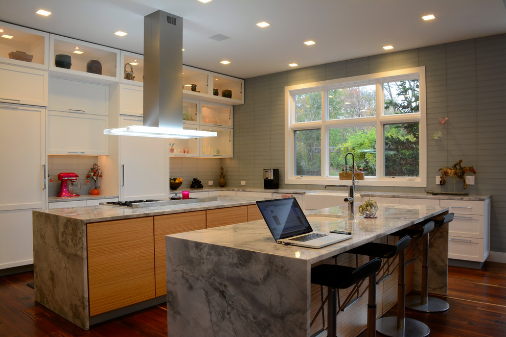 Design ideas for a large contemporary l-shaped open plan kitchen in Philadelphia with a farmhouse sink, shaker cabinets, white cabinets, marble benchtops, panelled appliances, medium hardwood floors, multiple islands, grey splashback, glass tile splashback and brown floor.