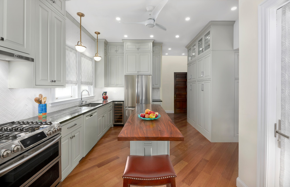Example of a transitional u-shaped medium tone wood floor and brown floor kitchen design in Phoenix with an undermount sink, raised-panel cabinets, gray cabinets, white backsplash, stainless steel appliances, an island and black countertops