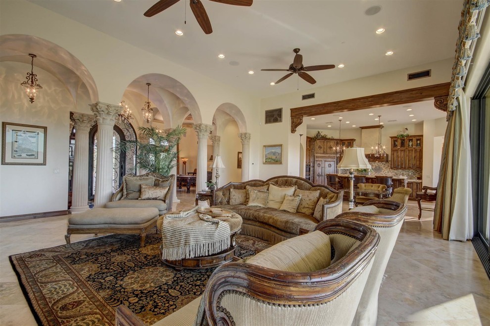 Photo of a large mediterranean open concept family room in Phoenix with travertine floors, beige walls, a standard fireplace, a plaster fireplace surround, a wall-mounted tv and beige floor.