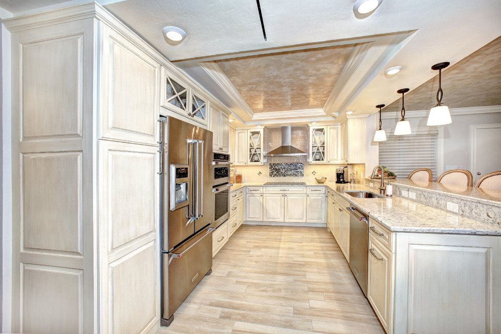 Photo of a large traditional u-shaped separate kitchen in Miami with an undermount sink, raised-panel cabinets, light wood cabinets, granite benchtops, stainless steel appliances, light hardwood floors, a peninsula, brown floor, grey benchtop and recessed.