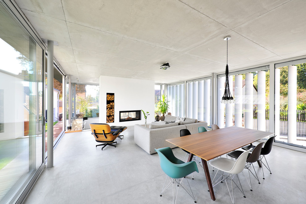 This is an example of a mid-sized industrial open concept living room in Nuremberg with a library, white walls, concrete floors, a two-sided fireplace, a plaster fireplace surround and grey floor.