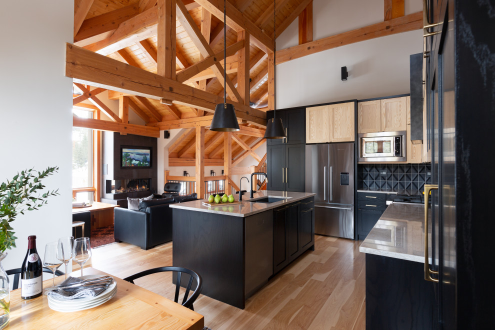 Example of a large transitional l-shaped light wood floor, brown floor and exposed beam eat-in kitchen design with a double-bowl sink, shaker cabinets, black cabinets, quartzite countertops, black backsplash, ceramic backsplash, stainless steel appliances, an island and gray countertops