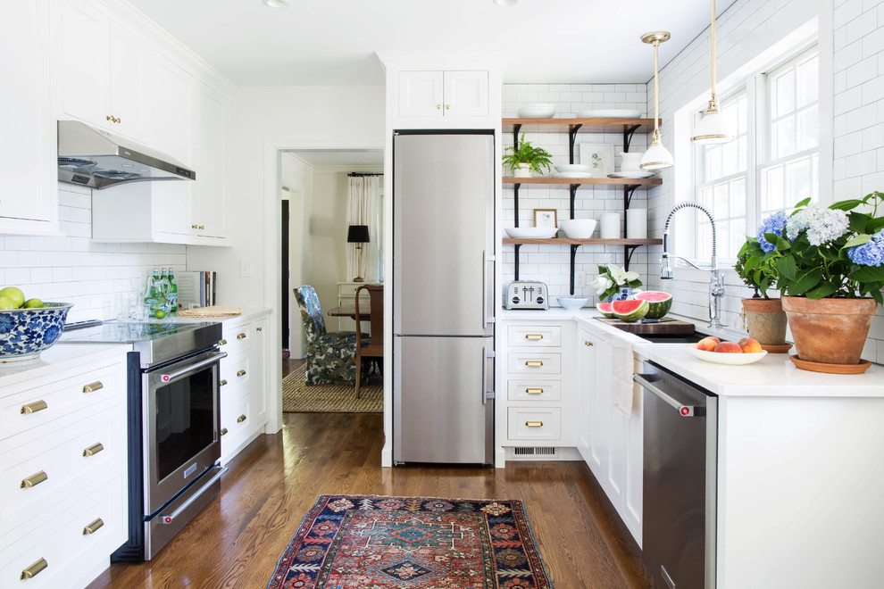 Transitional u-shaped medium tone wood floor and brown floor kitchen photo with an undermount sink, shaker cabinets, white cabinets, white backsplash, subway tile backsplash, stainless steel appliances and white countertops