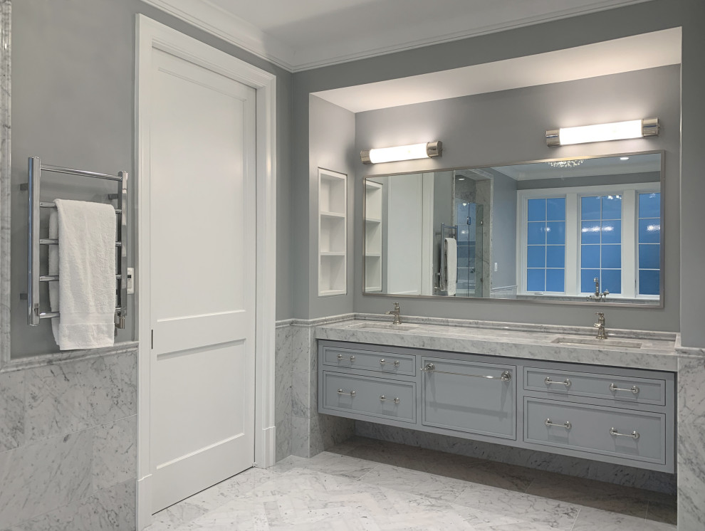 Idée de décoration pour une grande salle de bain principale et grise et blanche tradition avec un placard avec porte à panneau surélevé, des portes de placard bleues, une baignoire indépendante, un espace douche bain, WC à poser, un carrelage gris, du carrelage en marbre, un mur gris, un sol en marbre, un lavabo encastré, un plan de toilette en marbre, un sol gris, une cabine de douche à porte battante, un plan de toilette blanc, meuble double vasque, meuble-lavabo suspendu et un mur en pierre.