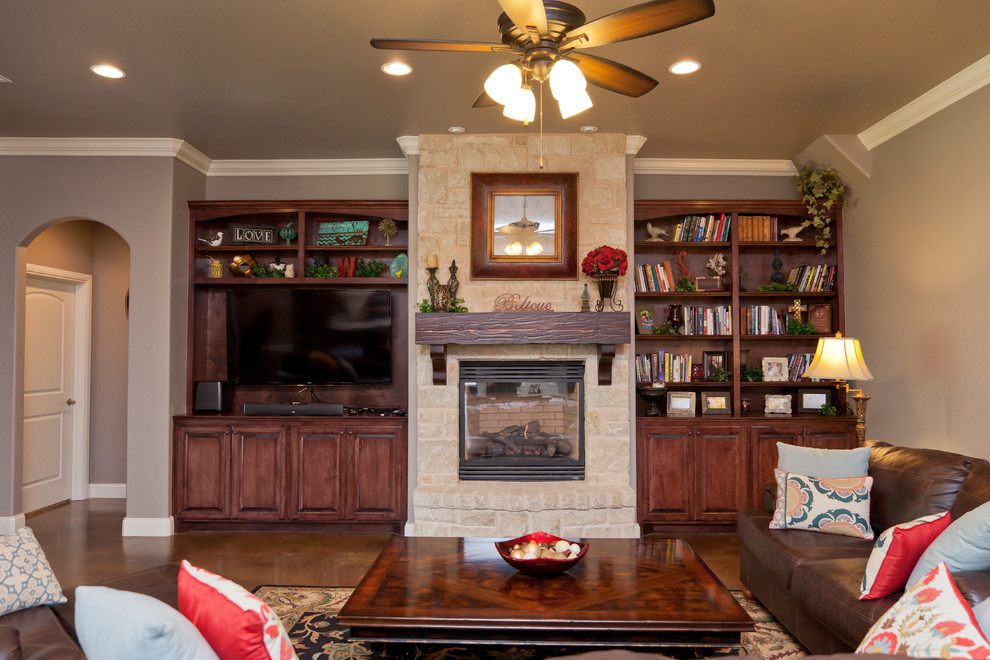 Mid-sized traditional open concept family room in Oklahoma City with a library, grey walls, concrete floors, a standard fireplace, a stone fireplace surround, a wall-mounted tv and brown floor.