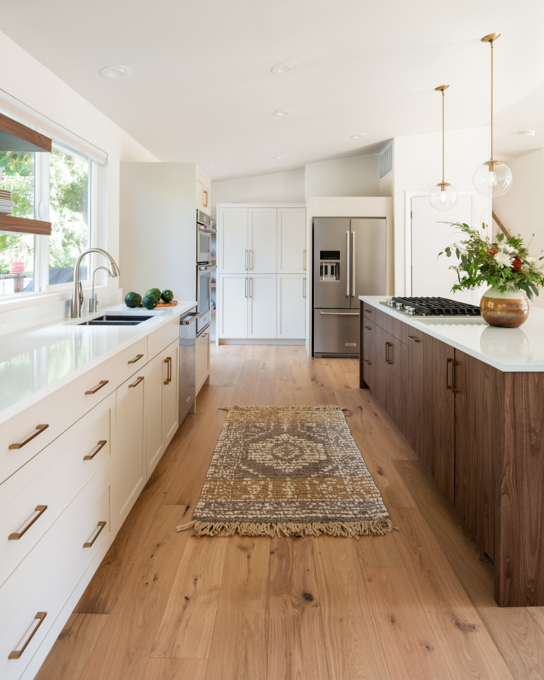 Photo of a large contemporary single-wall open plan kitchen in Seattle with a double-bowl sink, shaker cabinets, grey cabinets, quartz benchtops, white splashback, stainless steel appliances, light hardwood floors, with island, yellow floor and white benchtop.