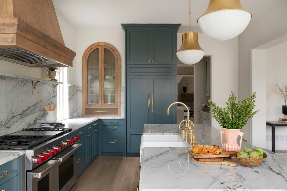 This is an example of an expansive traditional open plan kitchen in Minneapolis with a farmhouse sink, recessed-panel cabinets, blue cabinets, grey splashback, panelled appliances, light hardwood floors, with island, white benchtop, quartzite benchtops and stone slab splashback.
