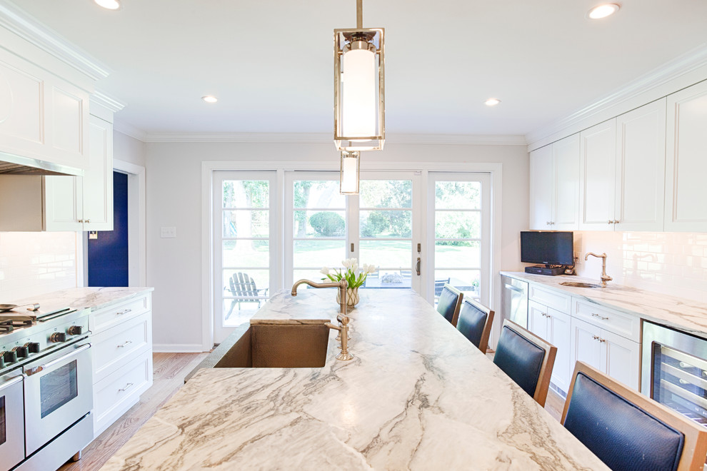 Large transitional l-shaped eat-in kitchen in Philadelphia with white cabinets, marble benchtops, white splashback, subway tile splashback, stainless steel appliances, medium hardwood floors, with island, a farmhouse sink and recessed-panel cabinets.