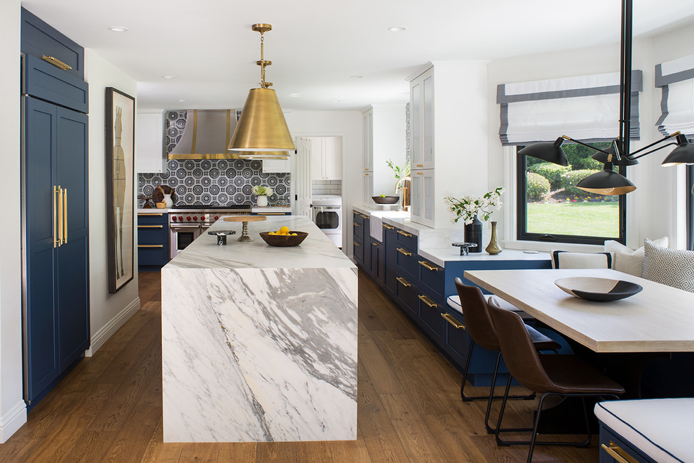 Large transitional u-shaped eat-in kitchen in Los Angeles with a farmhouse sink, shaker cabinets, blue cabinets, multi-coloured splashback, panelled appliances, medium hardwood floors, with island, brown floor, grey benchtop, marble benchtops and ceramic splashback.