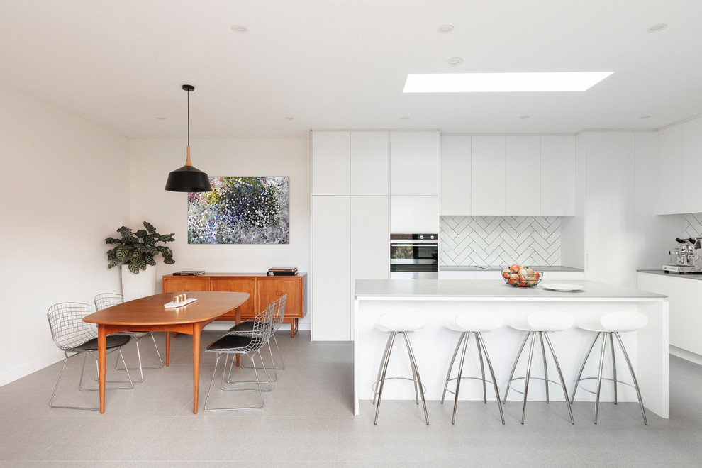 Photo of a contemporary l-shaped eat-in kitchen in Sydney with a double-bowl sink, white cabinets, subway tile splashback, terrazzo floors, with island, grey floor and grey benchtop.