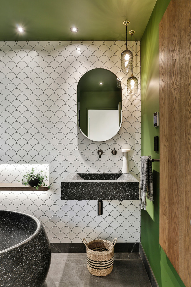 Inspiration for a mid-sized tropical 3/4 bathroom in Auckland with flat-panel cabinets, black cabinets, a freestanding tub, a curbless shower, a wall-mount toilet, white tile, ceramic tile, green walls, porcelain floors, a wall-mount sink, terrazzo benchtops, black floor, a hinged shower door and black benchtops.