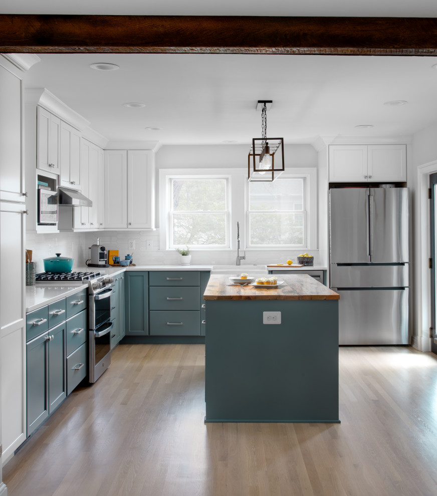Design ideas for a mid-sized transitional l-shaped kitchen in DC Metro with a farmhouse sink, shaker cabinets, green cabinets, quartz benchtops, white splashback, ceramic splashback, stainless steel appliances, light hardwood floors, with island, white benchtop and exposed beam.