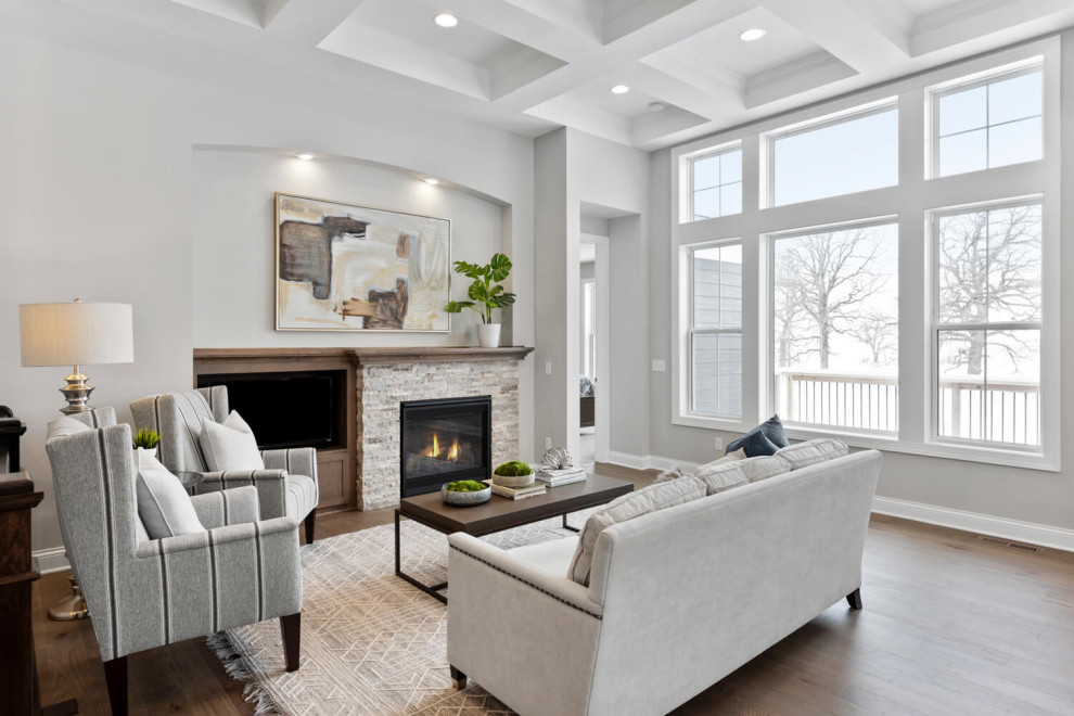 Offenes Klassisches Wohnzimmer mit grauer Wandfarbe, hellem Holzboden, Kamin, Kaminumrandung aus Stein und Kassettendecke in Minneapolis