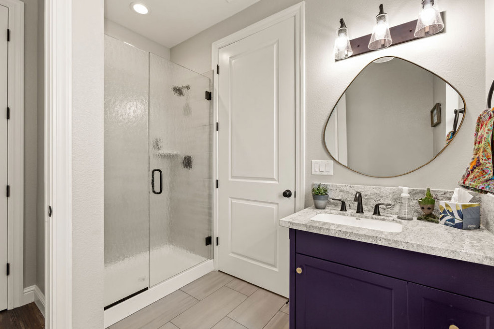 This is an example of a mid-sized modern kids bathroom in Sacramento with shaker cabinets, purple cabinets, an alcove shower, a one-piece toilet, grey walls, ceramic floors, a drop-in sink, granite benchtops, beige floor, a hinged shower door, grey benchtops, a single vanity and a built-in vanity.
