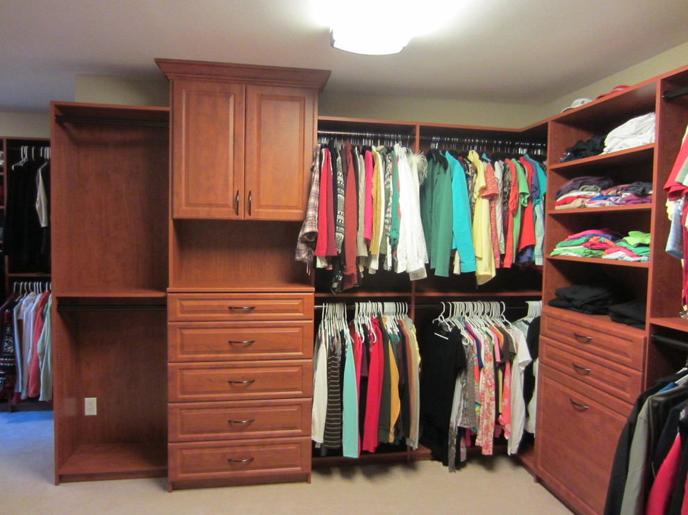 This is an example of a large traditional gender-neutral walk-in wardrobe in Other with raised-panel cabinets, medium wood cabinets and carpet.