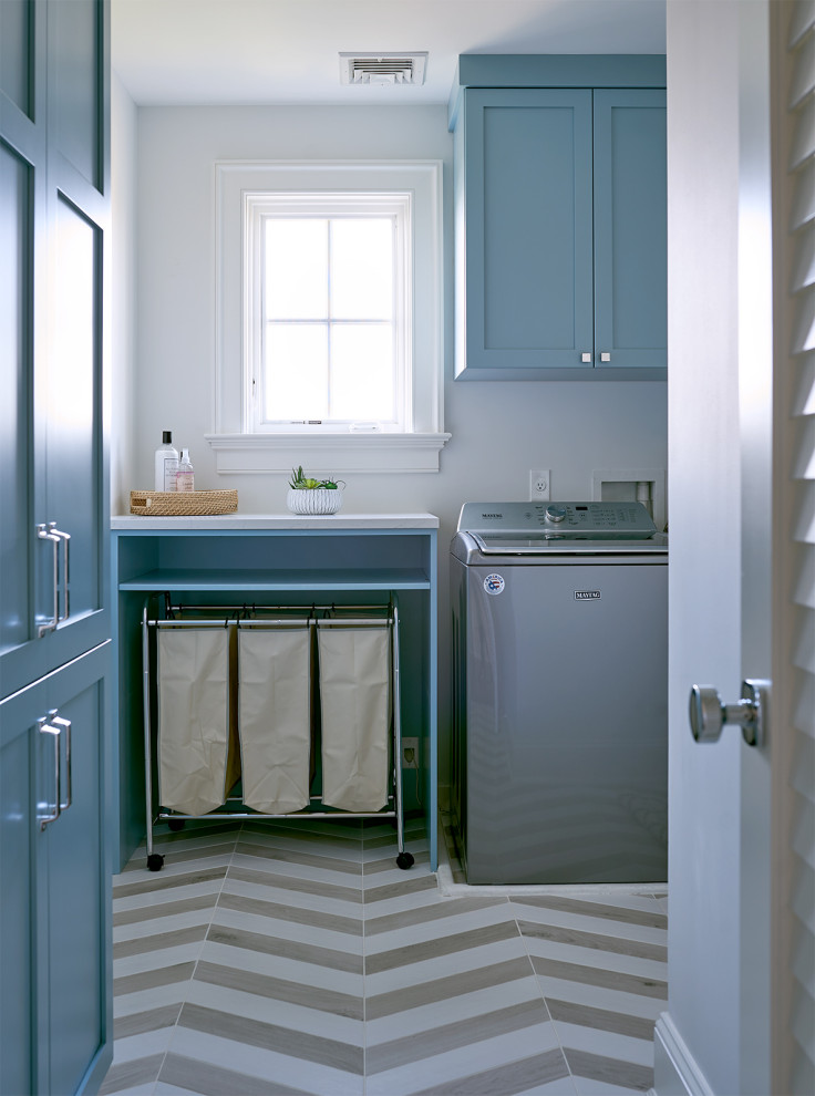 Design ideas for a large beach style l-shaped dedicated laundry room in New York with recessed-panel cabinets, blue cabinets, quartz benchtops, white walls, ceramic floors, a side-by-side washer and dryer, multi-coloured floor and white benchtop.