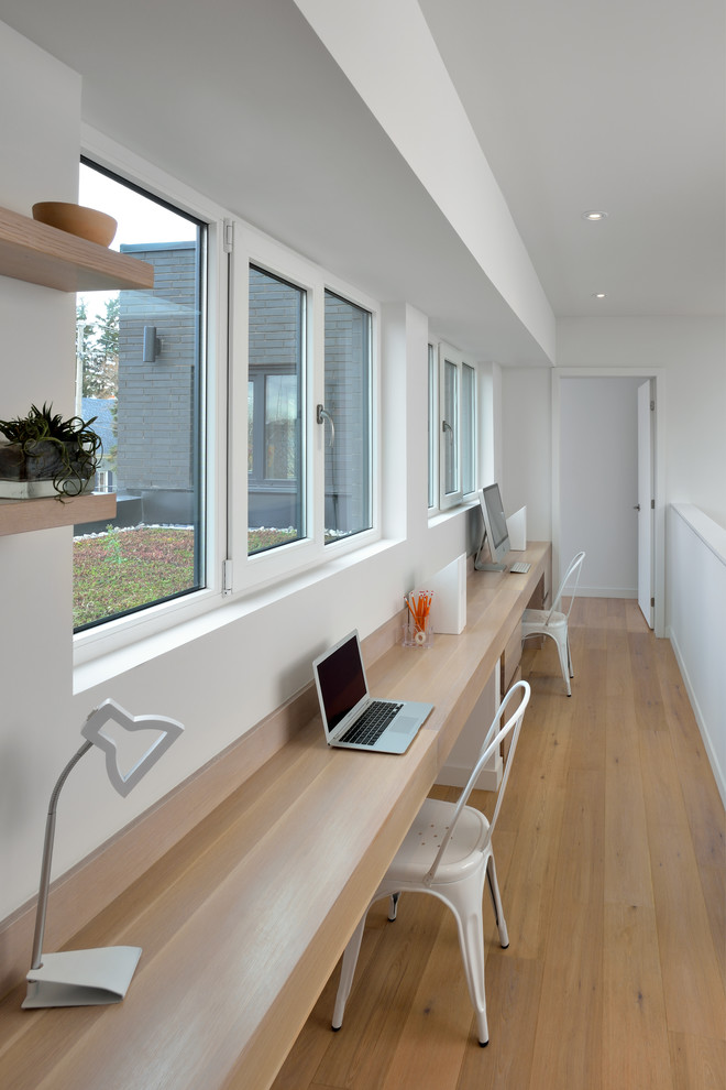 This is an example of a mid-sized contemporary study room in Toronto with white walls, light hardwood floors, a built-in desk and beige floor.