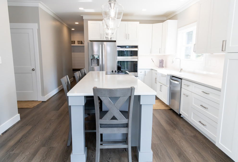 Bild på ett litet vintage vit linjärt vitt kök och matrum, med en nedsänkt diskho, luckor med profilerade fronter, vita skåp, marmorbänkskiva, vitt stänkskydd, rostfria vitvaror, vinylgolv, en köksö och brunt golv
