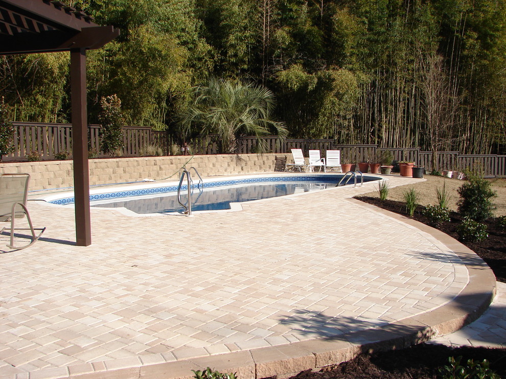 Photo of a mid-sized traditional backyard custom-shaped pool in Miami with brick pavers.