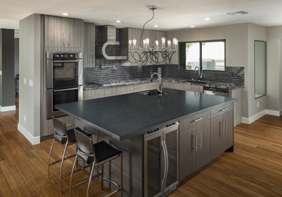 Photo of a large contemporary l-shaped open plan kitchen in Phoenix with an undermount sink, flat-panel cabinets, grey cabinets, granite benchtops, black splashback, stainless steel appliances, bamboo floors and with island.