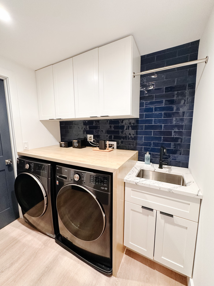 Foto di una piccola sala lavanderia costiera con lavello sottopiano, ante in stile shaker, ante bianche, top in quarzo composito, paraspruzzi blu, paraspruzzi con piastrelle in ceramica, pareti bianche, pavimento in vinile, lavatrice e asciugatrice affiancate, pavimento marrone e top bianco