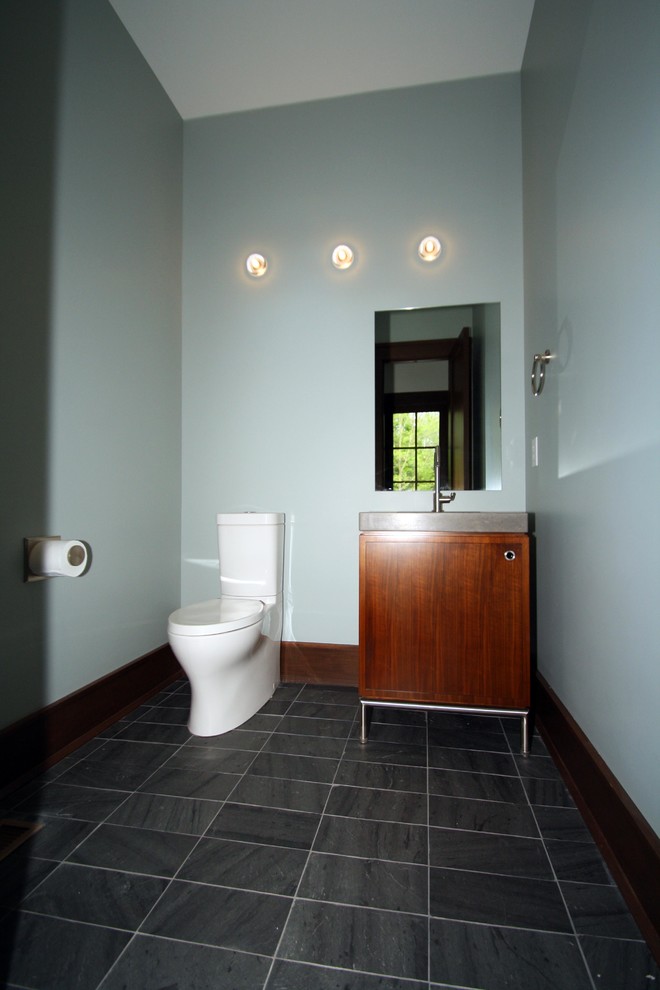 Inspiration for a small transitional powder room in Indianapolis with a wall-mount toilet, blue walls, flat-panel cabinets, medium wood cabinets, slate floors, an integrated sink, engineered quartz benchtops and grey floor.