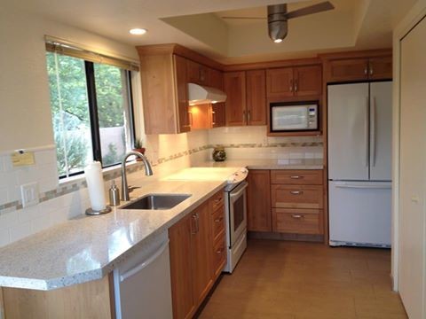 Photo of a mid-sized transitional l-shaped eat-in kitchen in Phoenix with an undermount sink, shaker cabinets, medium wood cabinets, recycled glass benchtops, white splashback, porcelain splashback and white appliances.