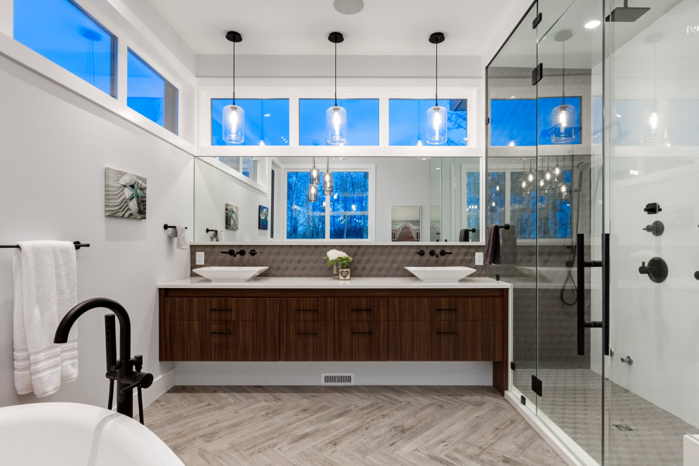 Photo of a contemporary bathroom in Calgary with flat-panel cabinets, dark wood cabinets, a freestanding tub, gray tile, grey walls, a vessel sink, grey floor, white benchtops and a double vanity.