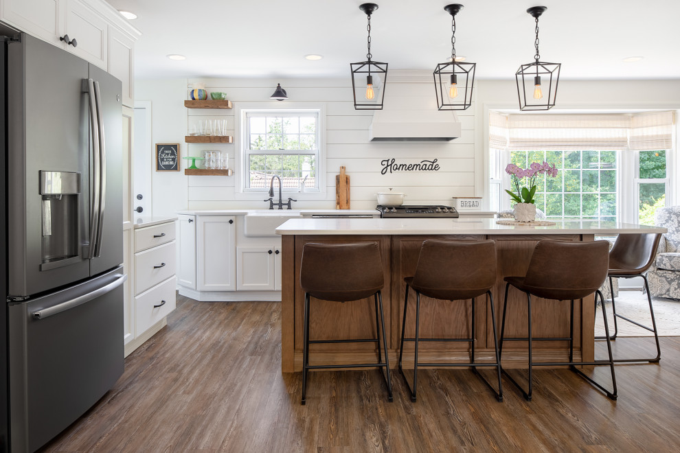 Photo of a mid-sized country l-shaped eat-in kitchen in Other with a farmhouse sink, shaker cabinets, white cabinets, quartz benchtops, white splashback, timber splashback, stainless steel appliances, vinyl floors, with island, brown floor and white benchtop.