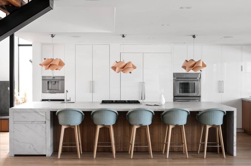 Mid-sized minimalist l-shaped medium tone wood floor and beige floor open concept kitchen photo in Orange County with an undermount sink, flat-panel cabinets, white cabinets, quartzite countertops, stainless steel appliances, an island and white countertops