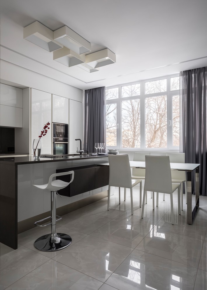 Inspiration for a contemporary galley eat-in kitchen in Other with flat-panel cabinets, white cabinets, black appliances, with island, black benchtop, black splashback and white floor.