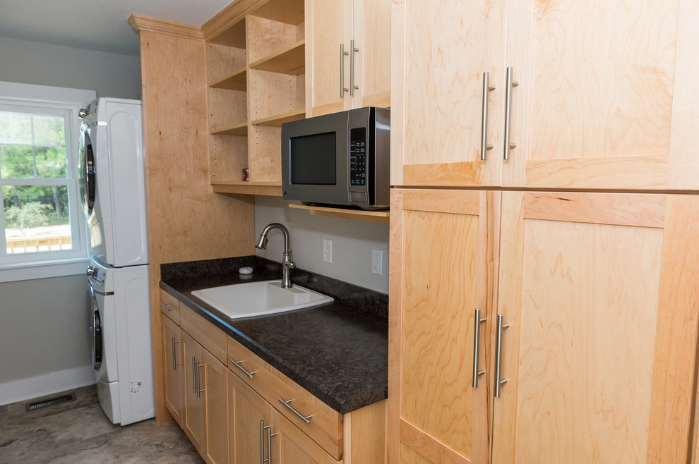 Transitional single-wall utility room photo with a drop-in sink, shaker cabinets, light wood cabinets, gray walls and a stacked washer/dryer
