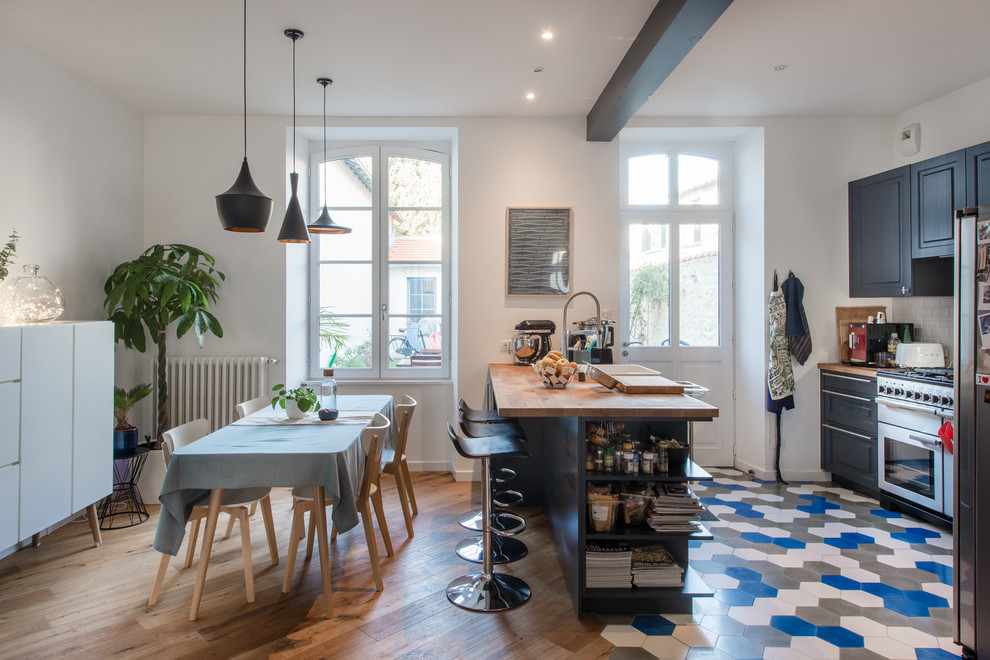 Scandinavian l-shaped eat-in kitchen in Montpellier with raised-panel cabinets, blue cabinets, wood benchtops, white splashback, subway tile splashback, stainless steel appliances, a peninsula, multi-coloured floor and brown benchtop.