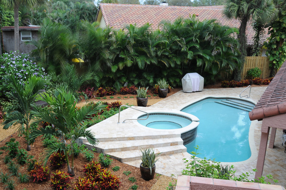 Photo of a mid-sized tropical backyard custom-shaped natural pool in Miami with a hot tub and natural stone pavers.
