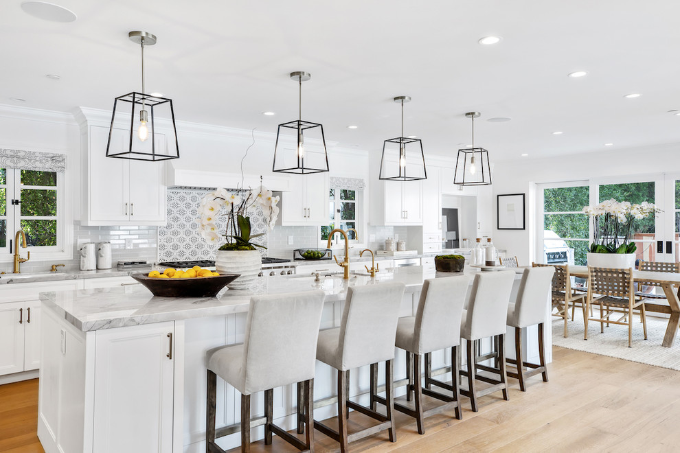 Photo of a beach style eat-in kitchen in Los Angeles with an undermount sink, shaker cabinets, white cabinets, multi-coloured splashback, stainless steel appliances, light hardwood floors, with island, beige floor and grey benchtop.