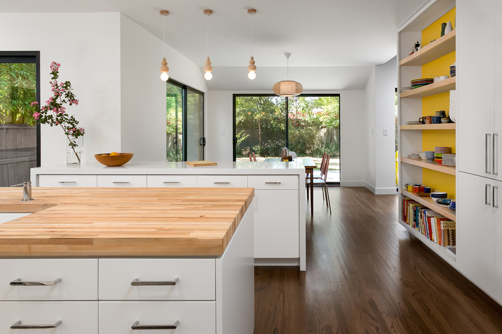 Mid-sized midcentury u-shaped eat-in kitchen in Los Angeles with a double-bowl sink, flat-panel cabinets, white cabinets, wood benchtops, yellow splashback, ceramic splashback, stainless steel appliances, medium hardwood floors, with island and brown floor.
