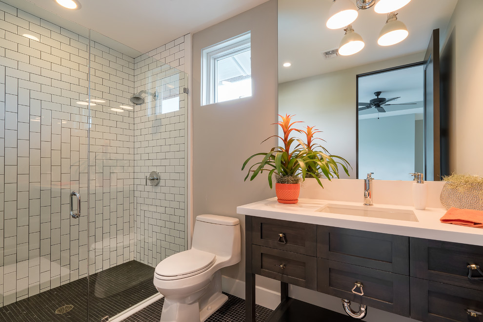 Small transitional bathroom in Orange County with shaker cabinets, black cabinets, an alcove shower, a one-piece toilet, white tile, grey walls, an undermount sink, solid surface benchtops, a hinged shower door, subway tile, mosaic tile floors and black floor.
