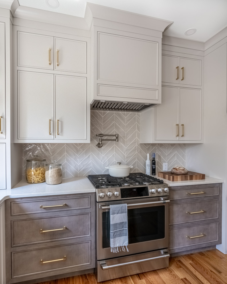 Photo of a mid-sized transitional l-shaped eat-in kitchen in Philadelphia with an undermount sink, flat-panel cabinets, beige cabinets, quartz benchtops, beige splashback, ceramic splashback, stainless steel appliances, dark hardwood floors, with island, brown floor and white benchtop.