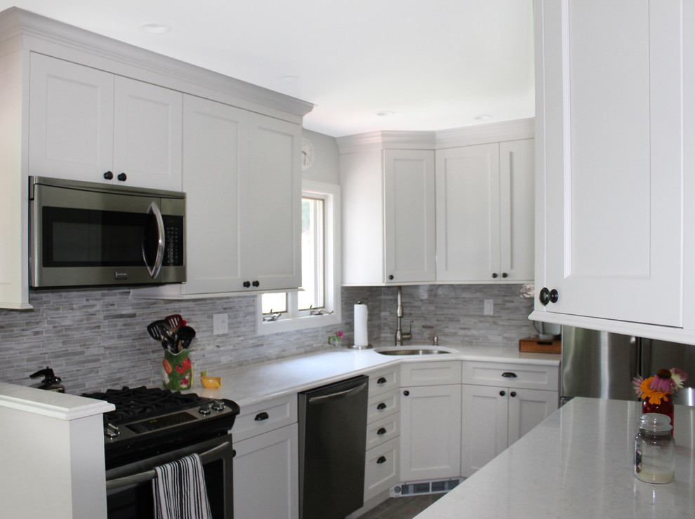 Mid-sized transitional galley light wood floor and brown floor enclosed kitchen photo in New York with an undermount sink, recessed-panel cabinets, white cabinets, marble countertops, beige backsplash, matchstick tile backsplash, stainless steel appliances and no island